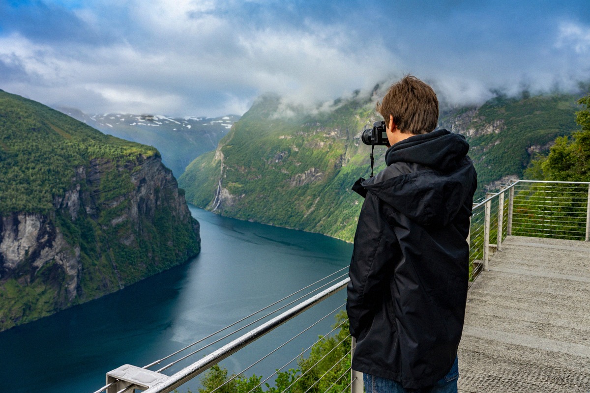 Ein Mann fotografiert von der Aussichtsplattform Ørnesvingen den Geirangerfjord